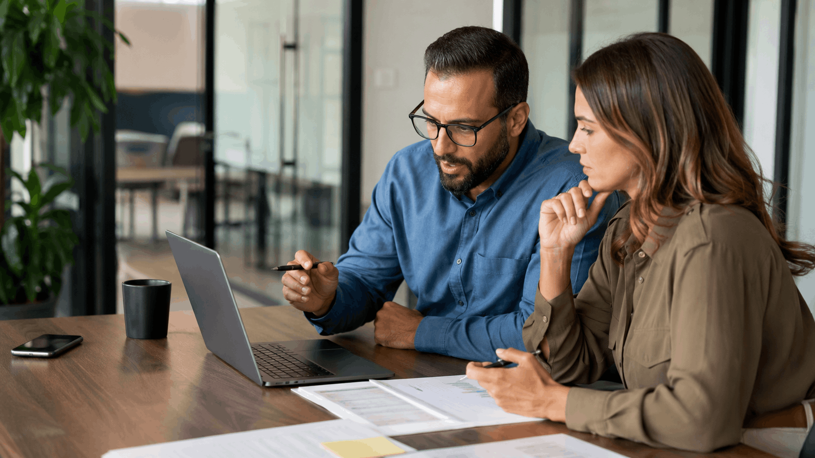 Two business professionals analyzing competitor search results on laptop in modern office